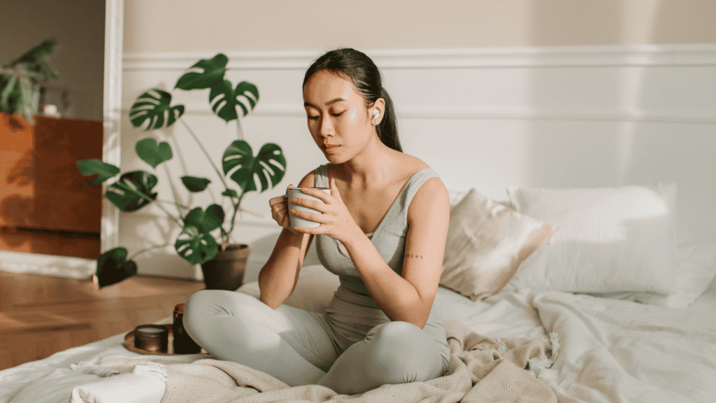 photo of asian girl doing self-care and wellness with cannabis and a cup of tea in bed. 