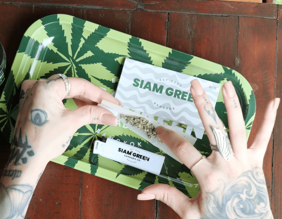 Hands packing pre-roll on Siam Green leaf-print rolling tray