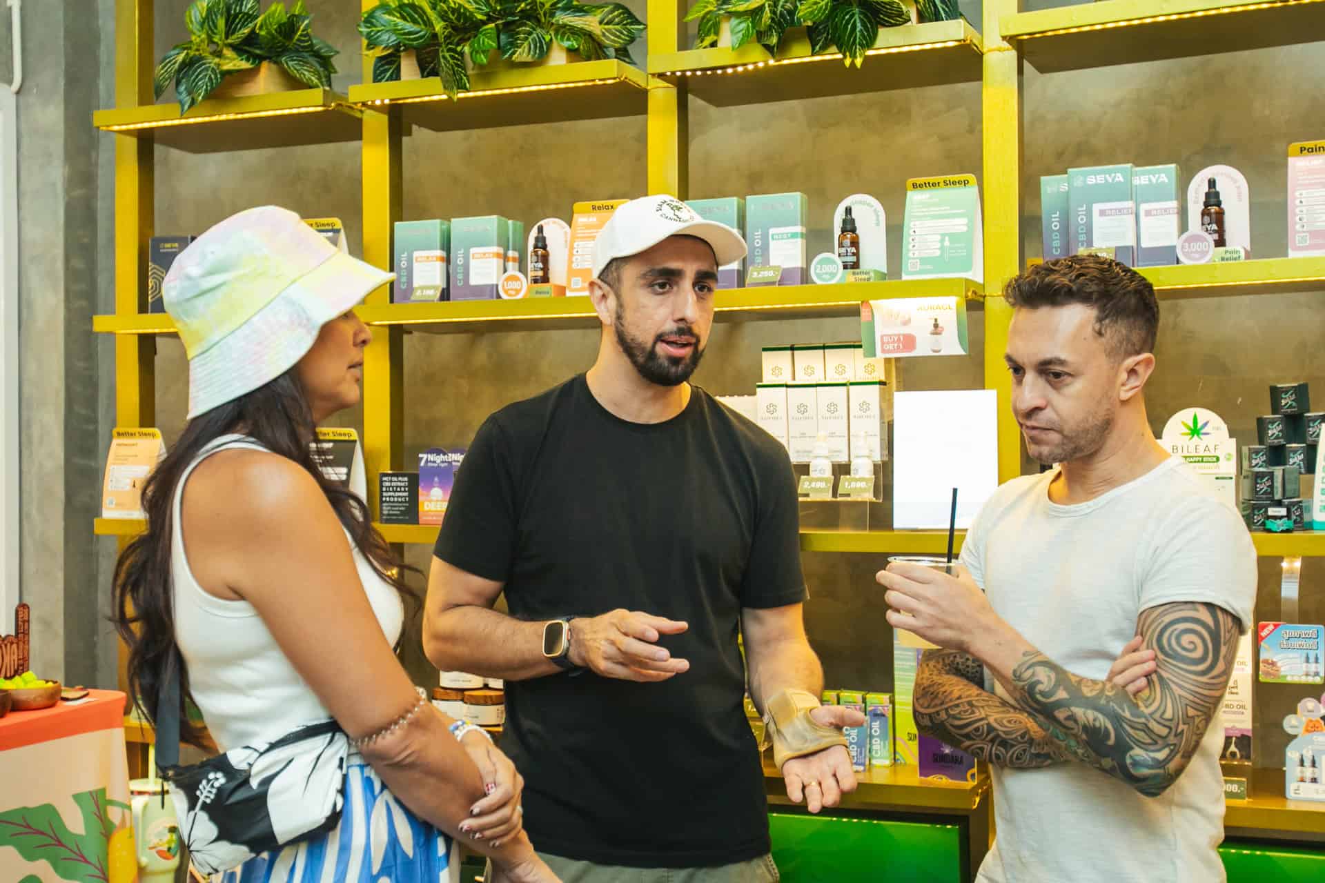 Siam Green budtender chatting with two customers beside CBD product shelves